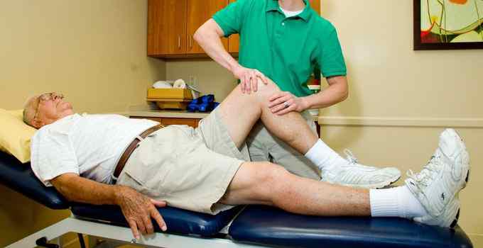 Physical therapist examining elderly man's knee.